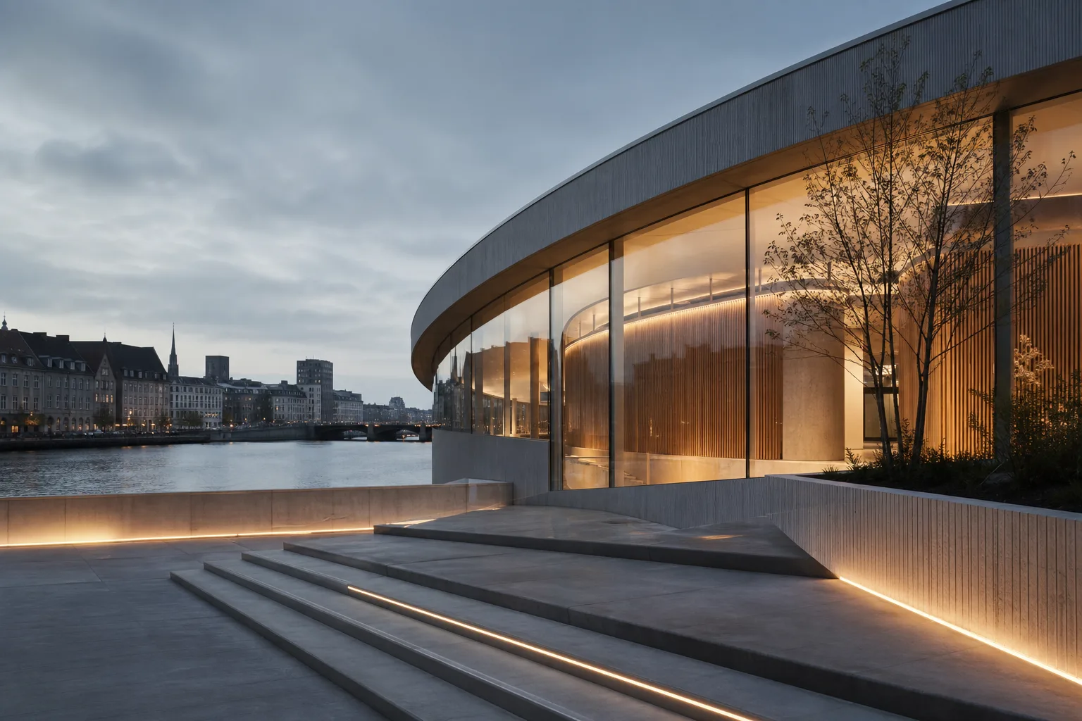 The Havnegade Pavilion at dusk: a curved glass building on the harbour, its fir-lined interior glowing warm above wide shallow steps, with the city on the far quay.